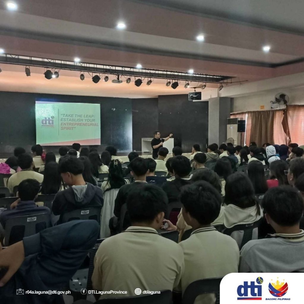 A resource speaker stands on stage presenting the session titled "Take the Leap: Establish Your Entrepreneurial Spirit" (visible on screen) to a large audience of seated participants during the DTI-Laguna Seminar on Budget Management in Santa Rosa City.