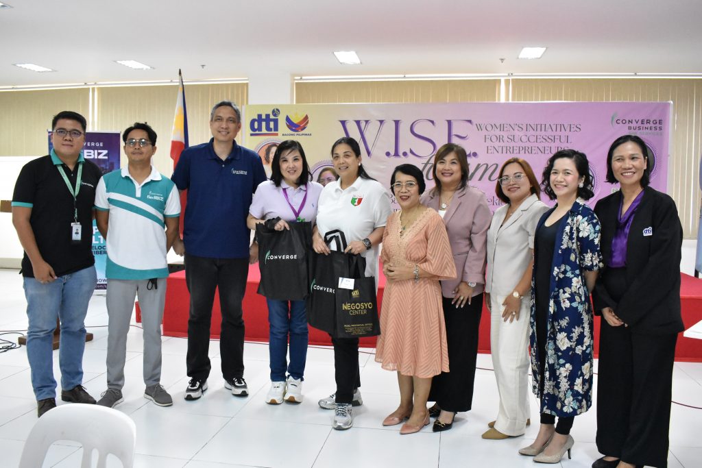 A group of people, mostly women, are standing in front of a banner that reads "DTI WISE WOMEN'S INITIATIVES FOR SUCCESSFUL ENTREPRENEUR CONVERGE BUSINESS". Some of them are holding Converge bags.