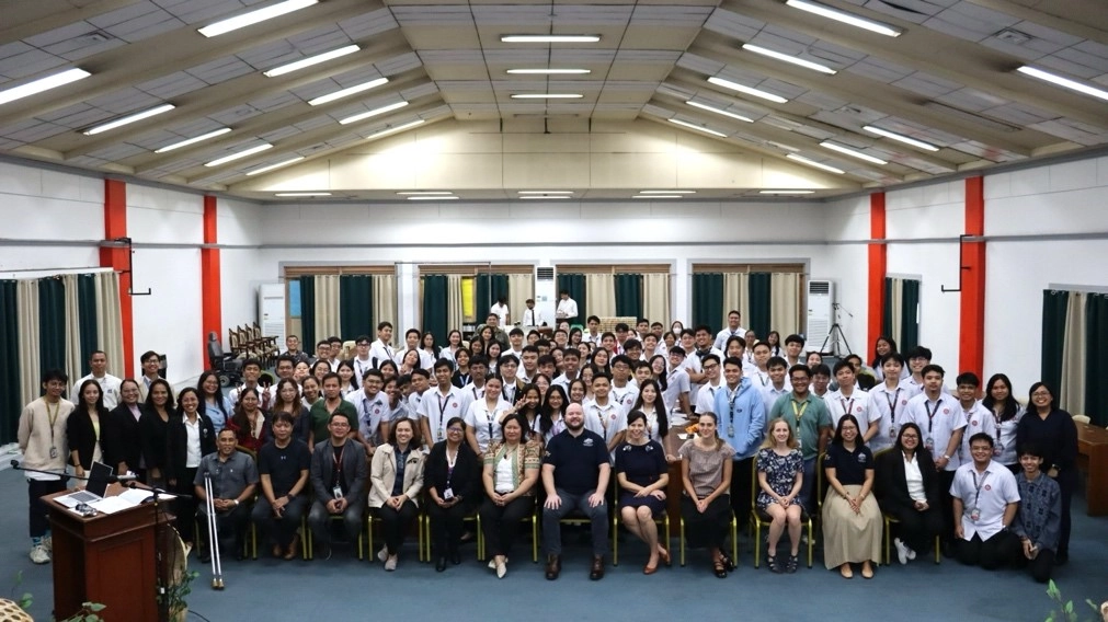 A large group of people, including DTI-BPS experts, Mr. Lachlan Parsons, Second Secretary of the Australian Department of Foreign Affairs and Trade, experts from Standards Australia, and Dr. Hasmin Ignacio, Vice President for Academic Affairs of the Technological University of the Philippines (TUP), are gathered in a spacious room with high ceilings and fluorescent lighting. The group consists of TUP faculty and students, all posing for a group photo during the CET-SEA University Roadshow.