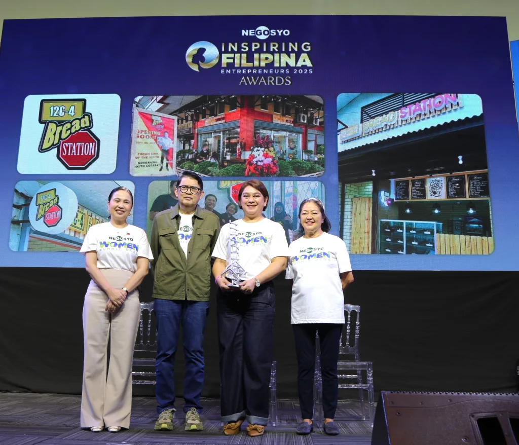 Four individuals stand on stage during the Go Negosyo Inspiring Filipina Entrepreneurs 2025 Awards. A woman in the center holds a trophy, while behind them, a large screen displays images of a business named "Bread Station." The group includes First Lady Liza Araneta-Marcos, DTI Secretary Cristina A. Roque, Go Negosyo Founder Joey Concepcion, and an award-winning Filipina entrepreneur.