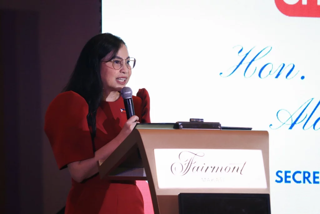 DTI Secretary Cristina A. Roque, wearing glasses and a red Filipiniana top, speaks at a lectern with a microphone during the Philippines-France Business Forum.
