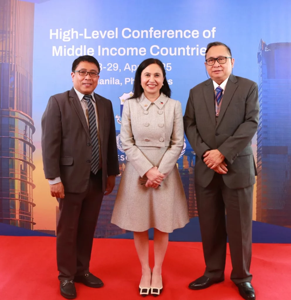 Three individuals are posing for a photo in front of a backdrop that reads "High-Level Conference of Middle Income Countries" and "April 28-29, 2025 Manila, Philippines." The person in the center is DTI Secretary Cristina A. Roque, given her prominent role in the article about the conference held in the Philippines.