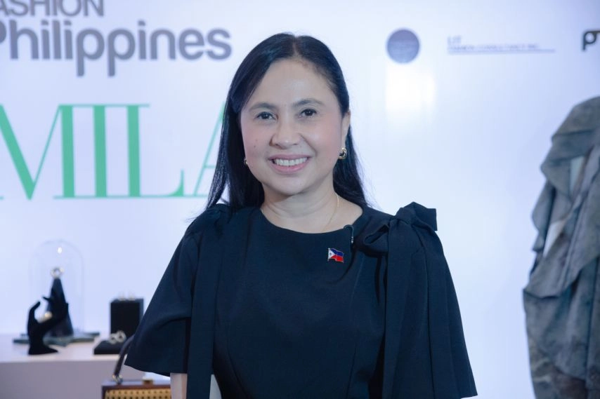Trade and Industry Secretary Cristina A. Roque stands in front of the FASHIONPhilippines Milan program backdrop, wearing a black outfit with a Philippine flag pin, as part of the DTI-CITEM initiative to promote Filipino design talent for Milan Fashion Week Spring/Summer 2026.