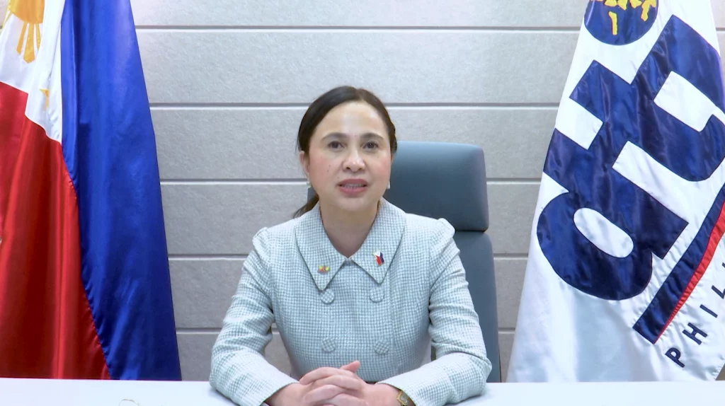 DTI Secretary Cristina A. Roque seated at a desk between the Philippine and DTI flags, delivering her recorded speech for the Philippine Innovation Hub Launch.