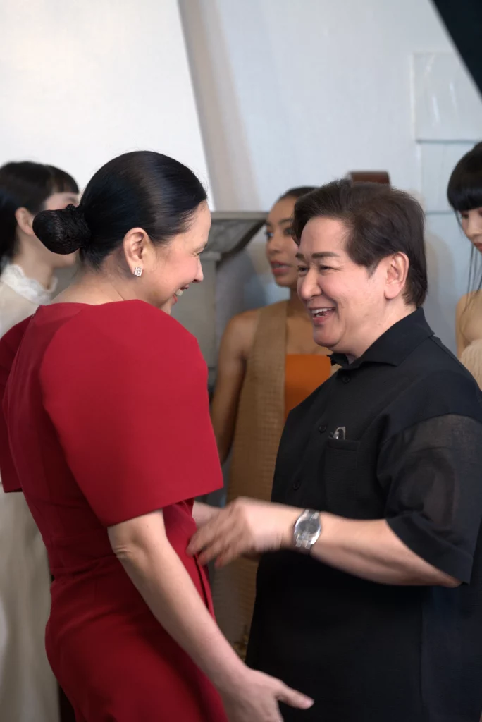 DTI Secretary Cristina Roque in a red dress and fashion designer Paul Cabral in black attire engaged in conversation during a formal event, with other attendees visible in the background.