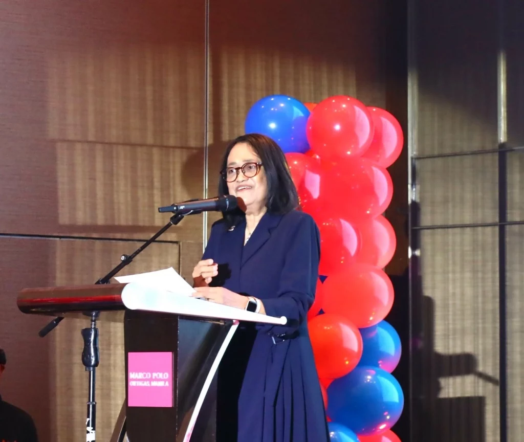 DTI Undersecretary Blesila Lantayona delivers a speech at the podium during the 7th Distributors Day at Marco Polo Ortigas Manila, with red and blue balloon columns in the background.