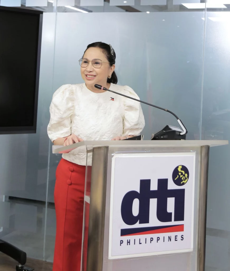 DTI Secretary Ma. Cristina A. Roque delivers a speech at the MOU signing event with Globaltronics, standing behind a podium with the DTI Philippines logo.