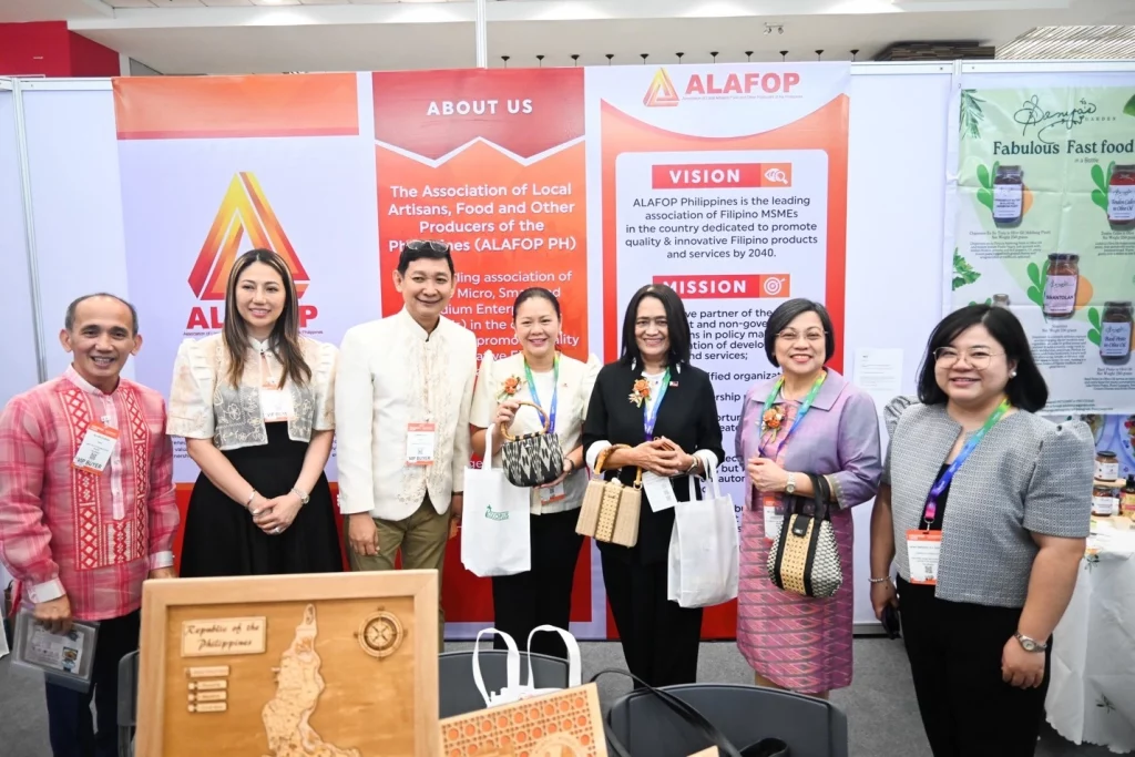 Usec. Blesila Lantayona with six other individuals at the ALAFOP booth during ProPak Asia 2025, standing in front of banners detailing the organization's vision and mission, with local products such as a wooden Luzon map and bags displayed on the table.