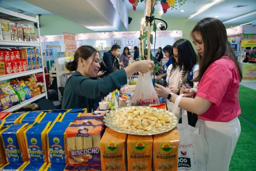 Visitors interact with vendors at a booth showcasing local snacks like Biscocho during Food Festival 2025 at SM Megamall, highlighting Filipino MSME products and culinary heritage.