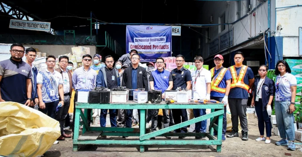 DTI officials and partner agency representatives stand in front of confiscated automotive batteries and electronic devices during the ceremonial destruction event at a wastewater treatment facility in Valenzuela City. The initiative reinforces the agency’s commitment to consumer protection and proper disposal of hazardous products.