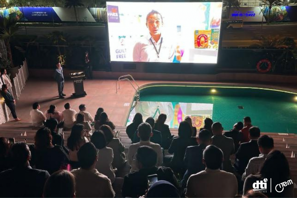 Audience members seated outdoors in front of a large screen displaying a CITEM presentation near a swimming pool, with a speaker at a podium addressing the audience. The event is part of CITEM's Appreciation Night activities held on February 17, 2025. The screen shows various images and text, including the words 'GUILT FREE.' The event is well-illuminated, and the audience is attentively watching the presentation.