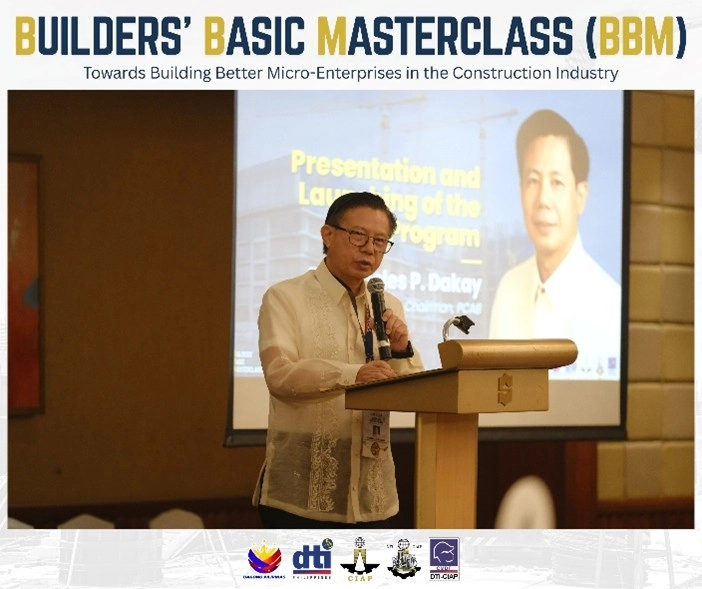 Engr. Jesse P. Dakay presenting at the Builders' Basic Masterclass (BBM) launch event, themed 'Towards Building Better Micro-Enterprises in the Construction Industry.' He stands at a podium with a screen behind him displaying the title 'Presentation and Launching of the Program,' along with logos of DTI, CIAP, and partner organizations.