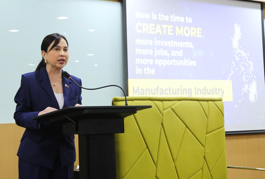 TI Secretary Cristina A. Roque delivering her speech at the CREATE MORE Forum, with event branding and a backdrop displaying the forum details.