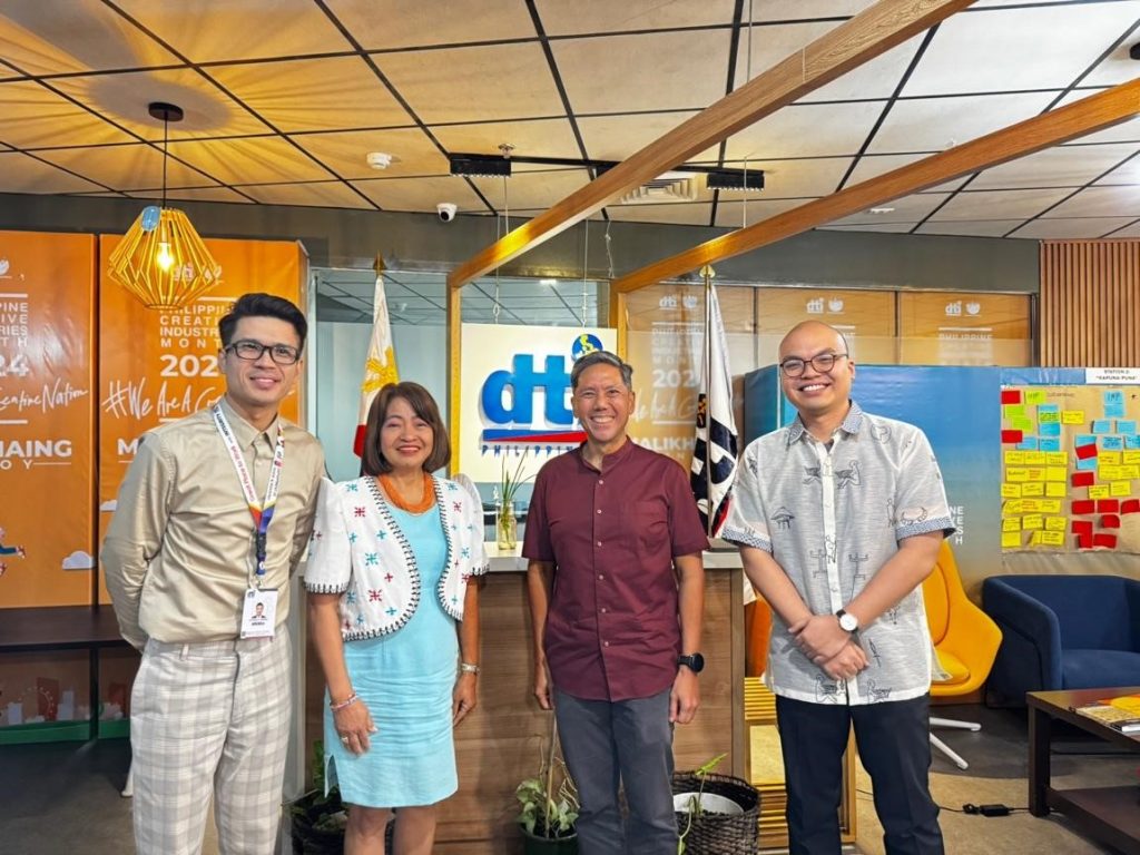 our Department of Trade and Industry officials stand in a line, smiling, in front of the DTI logo and Philippine flags. They are from left to right Assistant Director Jo-Dann N. Darong, Director Lilian G. Salonga, Paolo Mercado, and Atty. Gio Franco Gomez. A banner indicating the Philippine Creative Industries Month of 2024 is visible to the left.