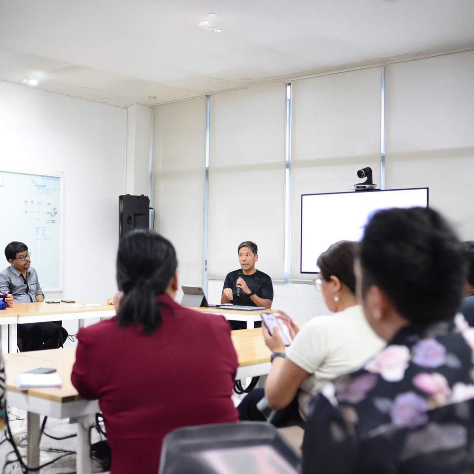 Paolo Mercado leads a meeting on Dumaguete's UCCN application. Group gathered around table in a bright room.