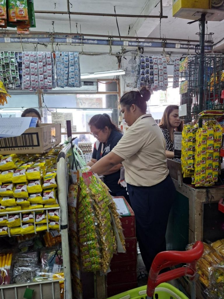 Customers and store staff engage in transactions inside a busy local store, as DTI monitors prices of basic goods in storm-affected areas to ensure compliance with the Price Act.