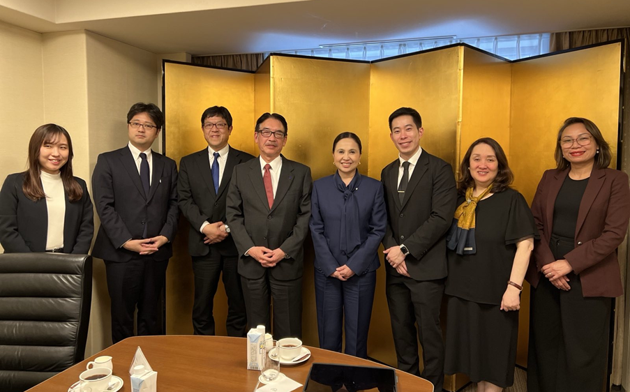 A group photo shows Department of Trade and Industry (DTI) Secretary Cristina A. Roque and several staff members, including DTI Assistant Secretaries Chua and Layug, and DTI-PTIC Tokyo STR Dita Angara-Mathay, posed with Japanese business representatives including Mr. Shinji Fukami, Senior General Manager of International Business Division, Mr. Masao Osumi, General Manager, and Ms. Narumi Saito & Mr. Hidetaka Yamanokuchi from the International Business Division. They stand in a room with a gold folding screen backdrop. In front of them on the table are cups of coffee and refreshments.