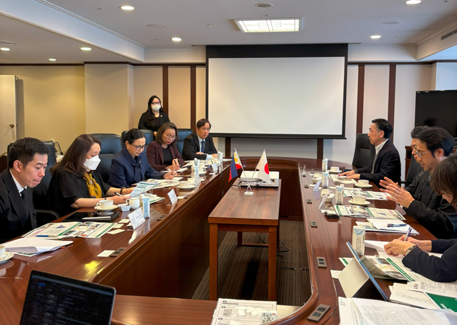 A bilateral meeting between the Department of Trade and Industry (DTI) Philippines and Chodai Co. Ltd. of Japan. DTI Assistant Secretary Englebert Josef Chua, Special Trade Representative Dita Angara-Mathay, and DTI Assistant Secretary May Niña Celynne Layug sit on one side of a long conference table. Opposite them sit members of Chodai Co. Ltd., including Mr. Yuji Munehiro, Mr. Masahiko Kato, and Mr. Junichiro Minobe. Both sides are reviewing documents, with the Philippine and Japanese flags displayed in the center of the table. 