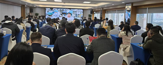 A wide shot of a room filled with seated individuals, who appear to be business representatives, possibly of East Asian descent, attending a presentation. They are facing a large screen displaying a video or presentation, where a person, possibly Director General Tereso Panga of the Philippine Economic Zone Authority (PEZA), is visible. The caption indicates that this is one of the investment promotion sessions co-organized by PEZA and PTIC Guangzhou with Aboitiz InfraCapital. The room appears to be a conference or meeting space, with blue and white chairs arranged in rows. The lighting is bright, and the overall atmosphere suggests a professional or business-oriented event. The individuals are dressed in business casual or formal attire. The image appears to be taken from the back of the room, showing the audience and the screen.