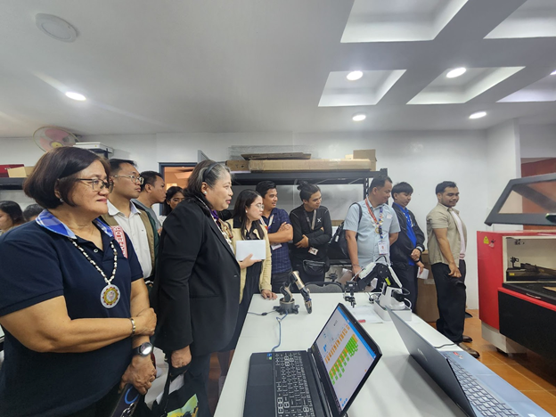 Group of individuals inside the CIT-U AI FabLab, surrounded by digital fabrication equipment including a laptop displaying data and a laser cutter, during the facility’s launch event.
